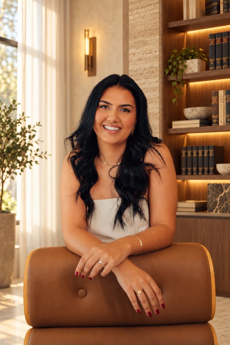 Salwa Muha Orabi sorrindo, com os braços apoiados no encosto de uma poltrona de couro, em uma sala com estantes de livros.
